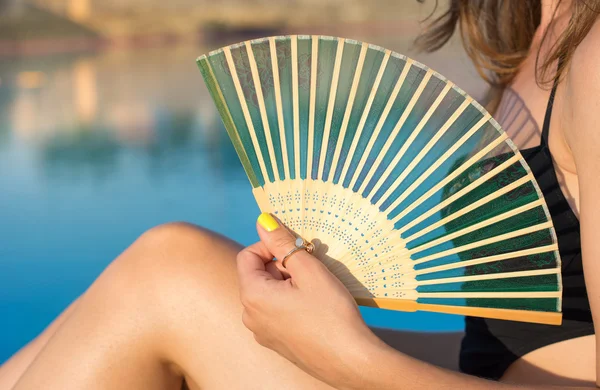 Girl in bikini holding a hand fan by the pool — Stock Photo, Image