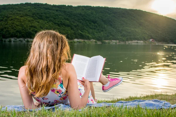 Uma rapariga a ler um livro junto ao lago. Divertimento de verão — Fotografia de Stock