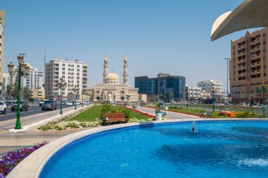 Sharjah, United Arab Emirates - March 24, 2021:Zahra mosque and Sharjah Clock Tower fountain emirate downtown in the United Arab Emirates low angle view clipart