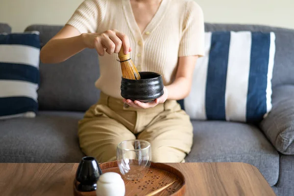 女人在家里用传统的茶道竹子和天然威士忌搅拌日本马沙绿茶饮料 同时坐在沙发上 — 图库照片