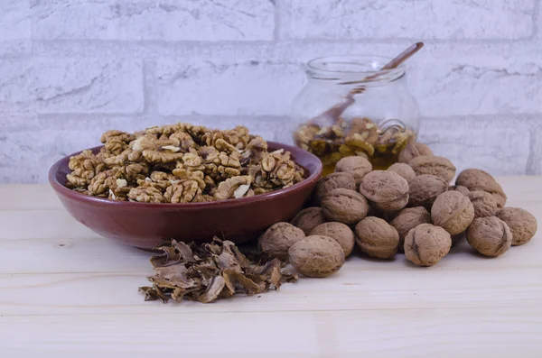 Whole and broken walnuts and a jar of honey — Stock Photo, Image