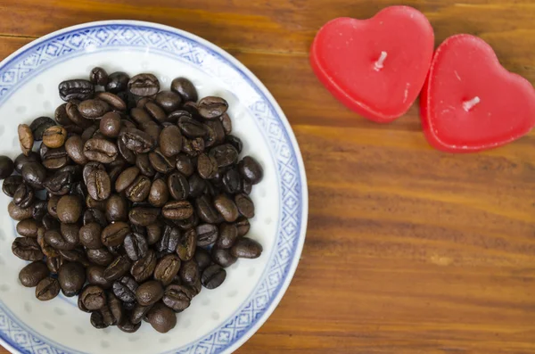 Coffee beans on a plate with heart shaped candles — Stock Photo, Image