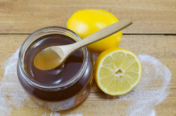 Jar of dark honey a wooden spoon and lemons — Stock Photo, Image