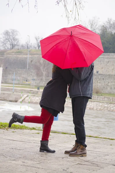 Pareja besándose detrás de una umbrela roja —  Fotos de Stock