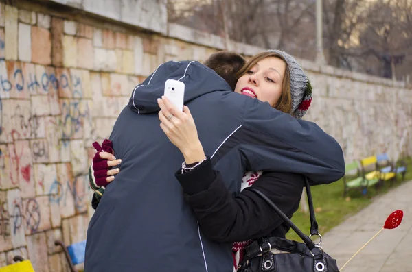 Chlapec objímat dívku, zatímco ona se dívá na její smartphone — Stock fotografie