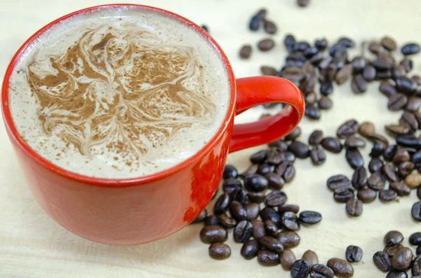 Червона чашка кави з прикрашеною піною та кавовими зернами — стокове фото