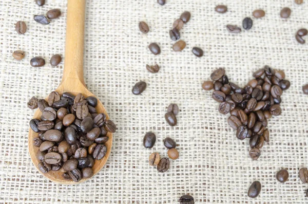 Cuchara de madera llena de granos de café tostados y un corazón de café — Foto de Stock