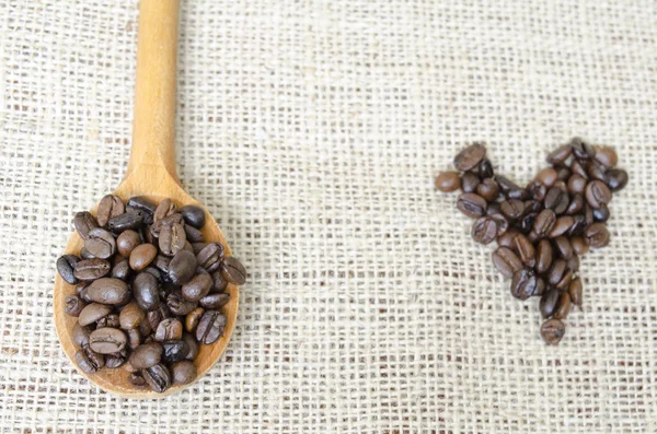 Wooden spoon full with roasted coffee beans and a coffee heart — Stock Photo, Image