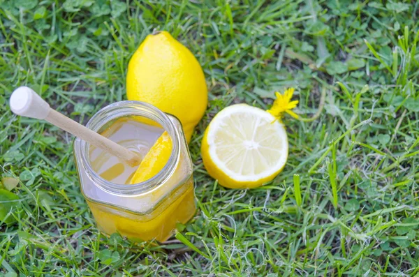 Sklenice medu, Naběračka, citron a žluté květy v trávě — Stock fotografie