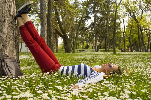 Gadis Bunette tergeletak di rumput dengan kakinya beristirahat di pohon — Stok Foto