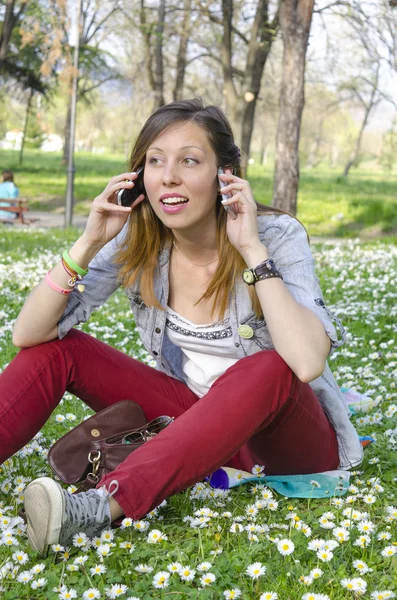 Brunett tjej pratar på två telefoner i gräset — Stockfoto