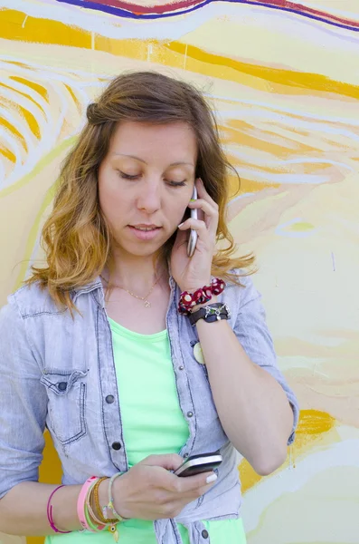 Девушка разговаривает по одному телефону во время чтения текстового сообщения — стоковое фото