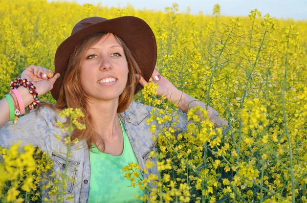 Vacker flicka poserar i ett fält av gula blommor — Stockfoto