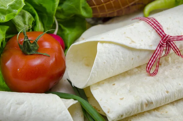 Wrapped empty tortillas on a table with tomato, lettuce and ham — Stock Photo, Image