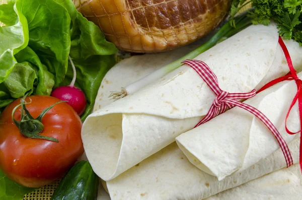 Wrapped empty tortillas on a table with tomato, lettuce and ham — Stock Photo, Image