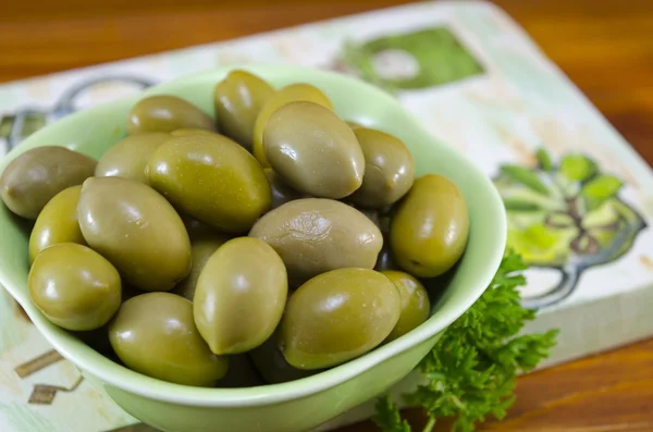 Olive verdi e prezzemolo crudo su un bordo decorato decoupage — Foto Stock