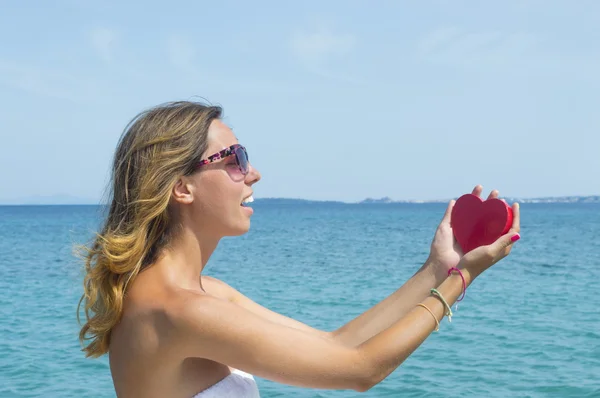 Young woman holding a heart shaped box at the seaside — Stock Photo, Image