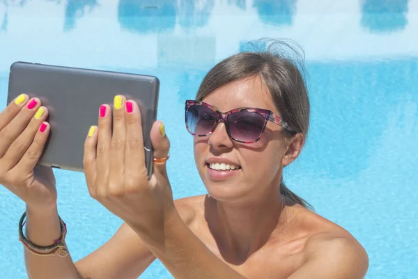 Молодая девушка делает селфи у бассейна с планшетом — стоковое фото
