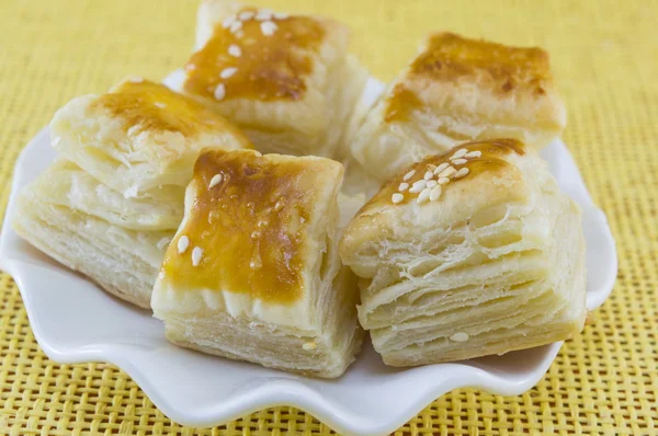 Puff pastry with sesame in a white plate on a yellow background — Stock Photo, Image