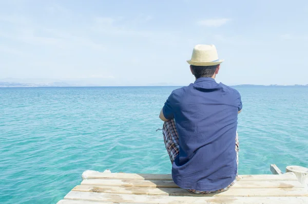 Young man sitting on the dock looking at blue sea — Stock Photo, Image