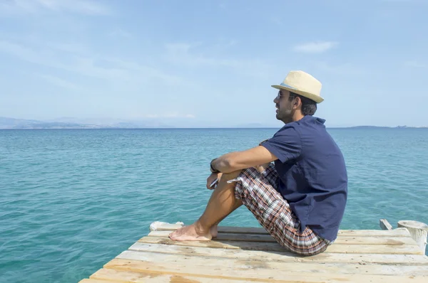 Young man sitting on the dock looking at blue sea — Stock Photo, Image