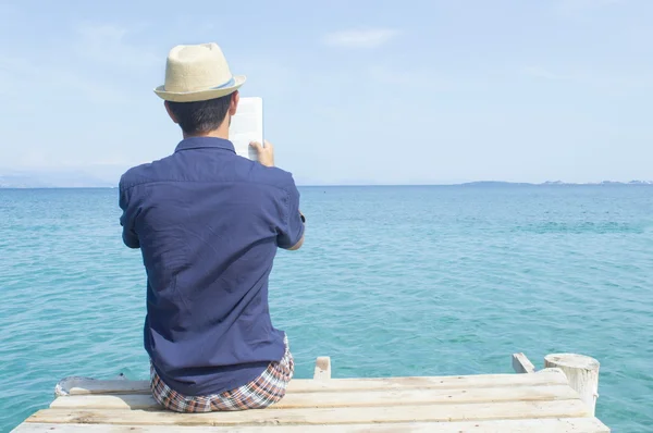 Young man sitting on the dock reading a book — Stock Photo, Image