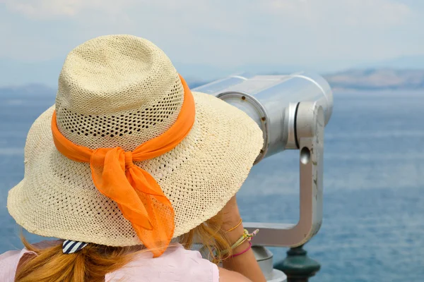 Menina olhando através de binóculos públicos à beira-mar vestindo rosa — Fotografia de Stock