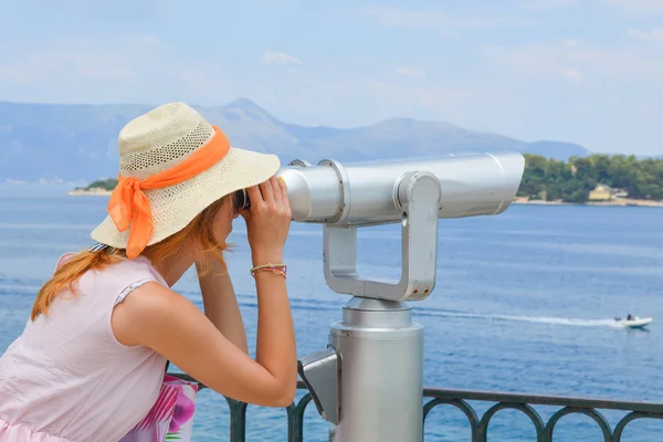 Girl looking thru public binoculars at the seaside wearing pink — Stock Photo, Image