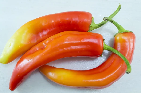 Fresh crooked orange and red peppers on a white wooden table — Stock Photo, Image