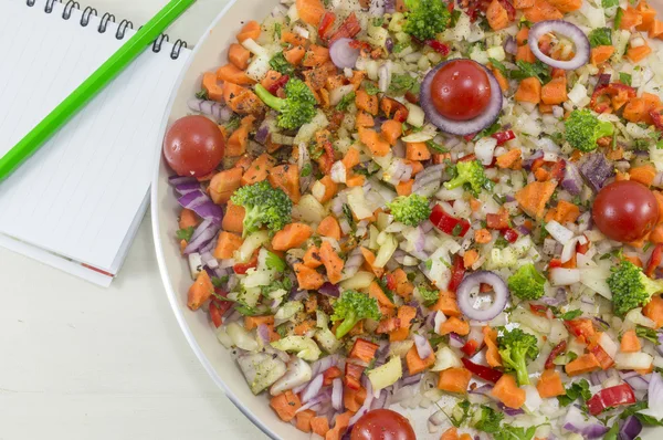 Ensalada de verduras en un plato junto a un cuaderno abierto y un bolígrafo para —  Fotos de Stock