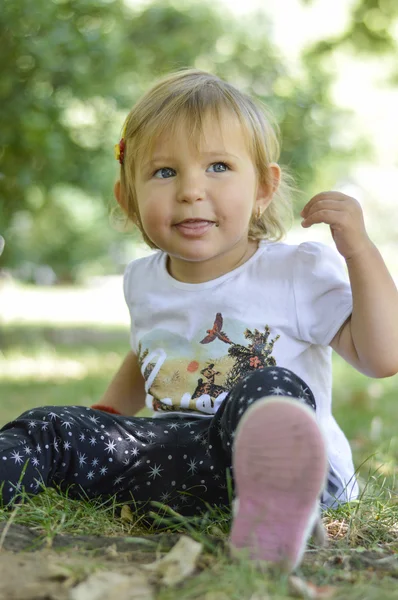 Linda niña de un año sentada en la hierba en un parque — Foto de Stock