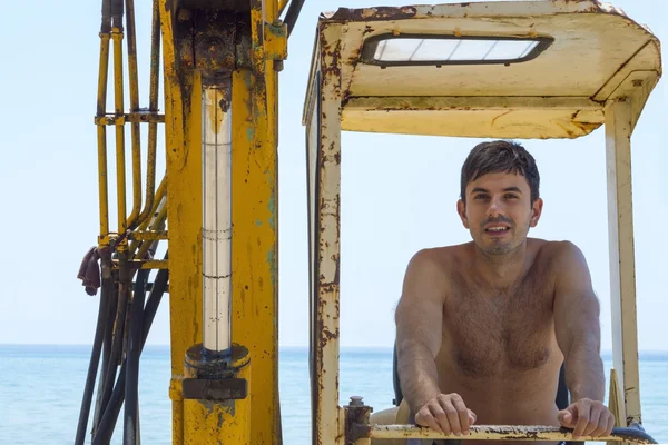 Young man sitting in a bulldozer at the beach — Stock Photo, Image