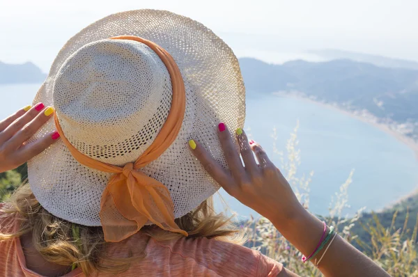 Girl wearing straw hat looking at the seaside from mountain view — Stock Photo, Image