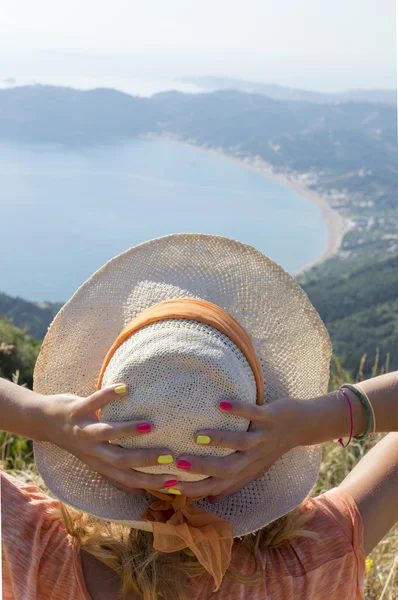 Girl wearing straw hat looking at the seaside from mountain view — Stock Photo, Image