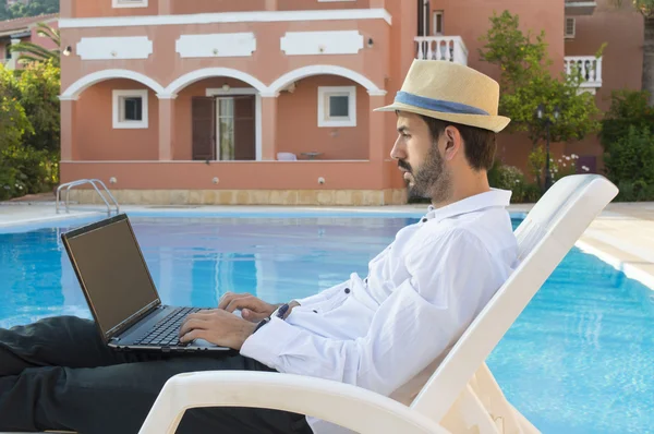 Young businessman working on his laptop by the pool while on vac