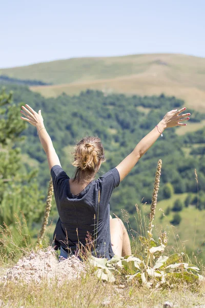 Young woman with backpack sitting on cliff's edge and looking to — Stock Photo, Image