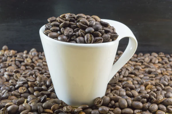 Taza de café blanco llena de granos de café colocados en coff tostado — Foto de Stock