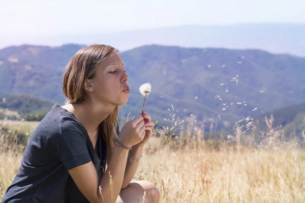 Morena menina soprando um dente de leão no campo — Fotografia de Stock