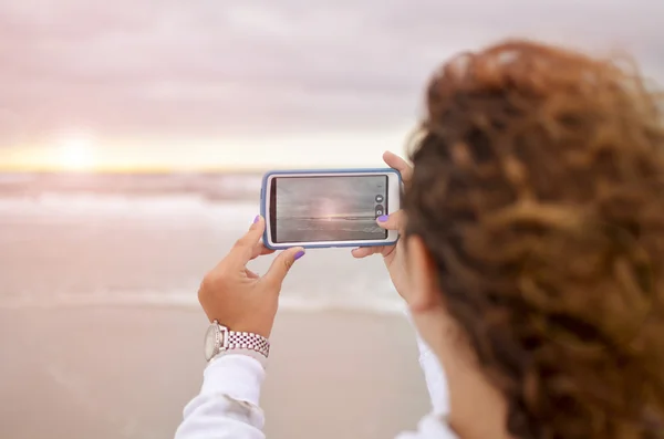 Menina encaracolado fotografar o nascer do sol no oceano — Fotografia de Stock