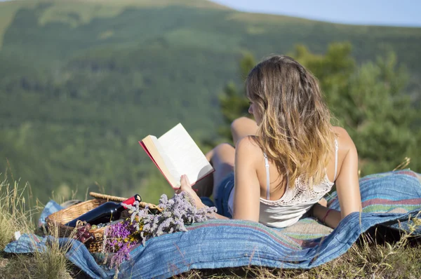 Giovane donna sdraiata su una coperta e leggere un libro su un pic-nic i — Foto Stock