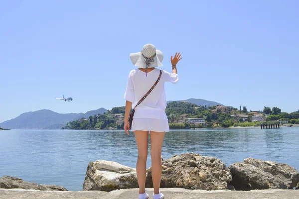 Mädchen winkt einem Flugzeug zu, das über Meer fliegt — Stockfoto