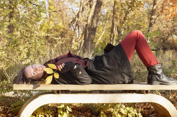 Vacker flicka liggande på bänken i parken färgade i höst colo — Stockfoto