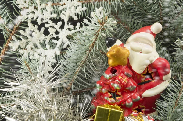 Juguete Santa entre abetos, regalos y copos de nieve . — Foto de Stock