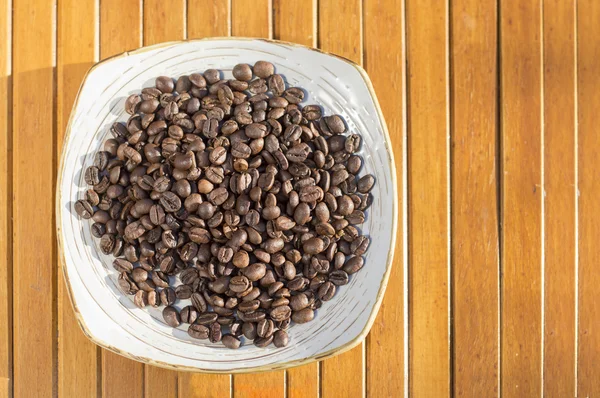 Granos de café en un plato sobre una mesa de madera — Foto de Stock