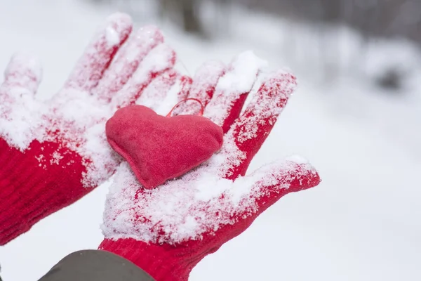 Luvas vermelhas cobertas de neve segurando um coração — Fotografia de Stock