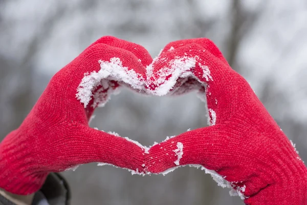 Luvas de lã vermelha fazendo uma forma de coração na neve — Fotografia de Stock