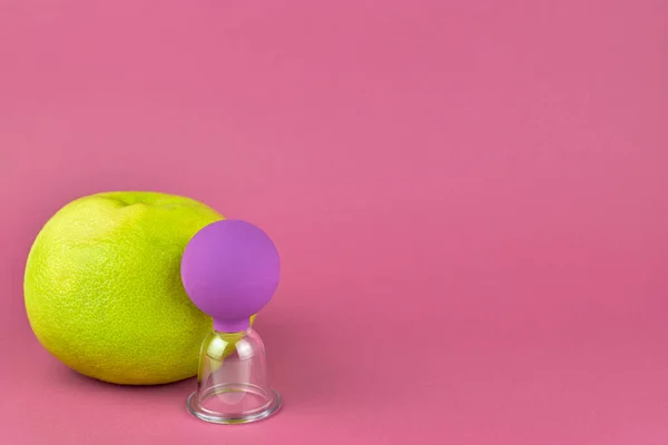 Cupping massage against cellulite. Orange and massage jar on a rose background, copy space. The concept of body care against cellulite at home.