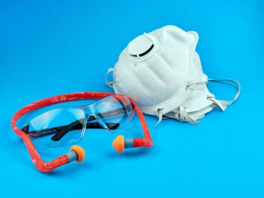 Kişisel koruyucu ekipman. İşçiler için PPE. Mavi arka planda toz maskeleri, güvenlik gözlükleri ve kulak tıkaçları..