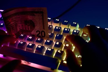 Hacker etiketli bir klavye ve bir dolar banknot. Finansal siber suç kavramı, internetteki dolandırıcılar. Hacker 'ın elleri klavyede ve parada. Parayı siber suçlulardan korumak..