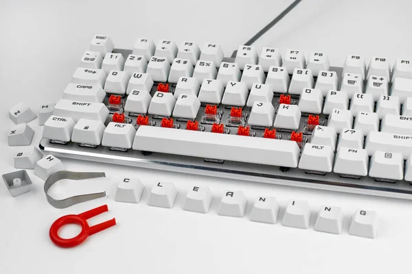 White mechanical keyboard with the keys removed. The concept of cleaning the keyboard. Maintenance of gaming equipment. The word Cleaning on the buttons.
